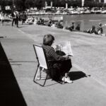 Femme assise sur un fauteuil pliant et lisant son jounral aux bains des Pâquis, Genève