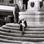 Homme assis sur les marches de la fontaine au bas de la rue de la Cité, Genève